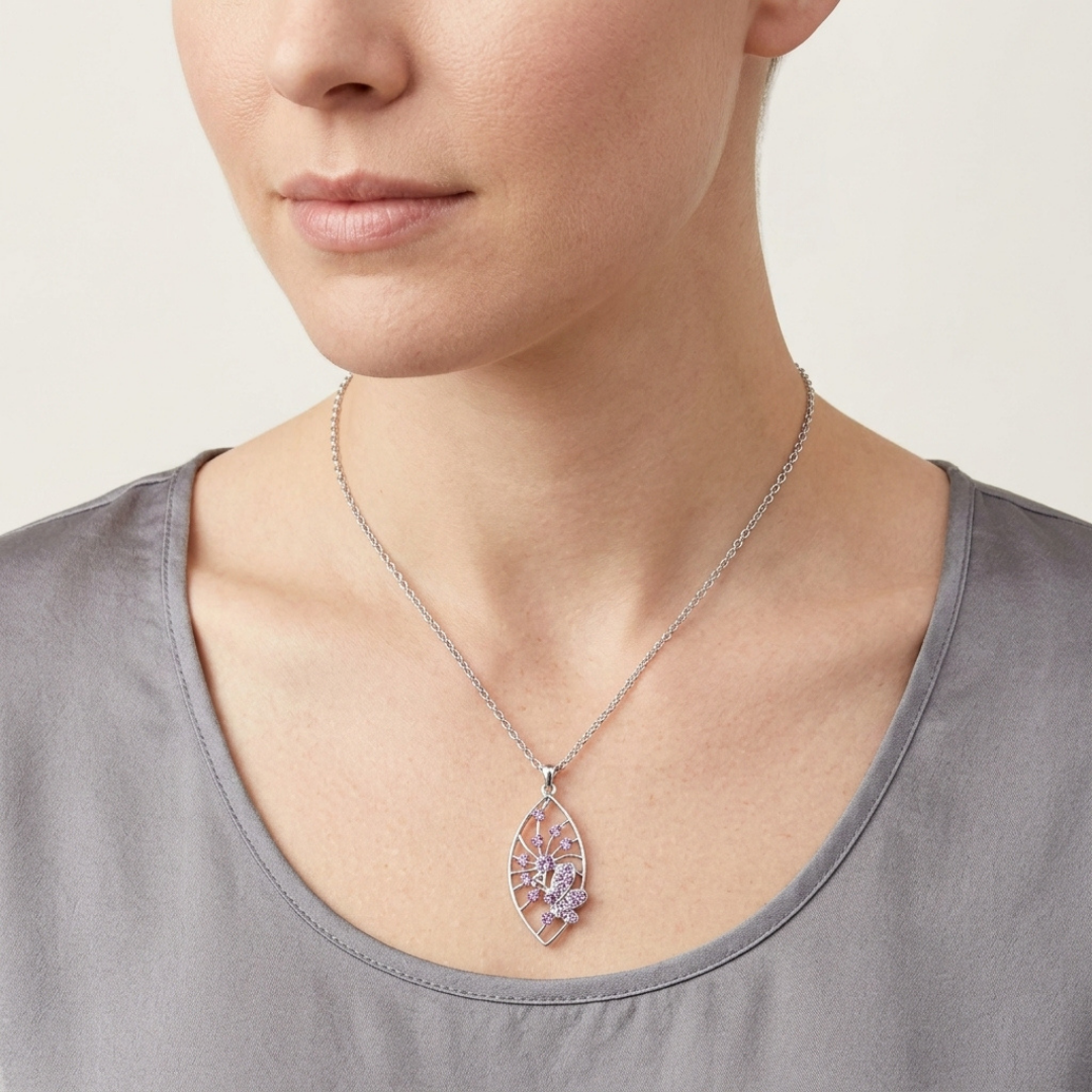 Person wearing a silver necklace with a light purple crystal butterfly pendant on a plain background