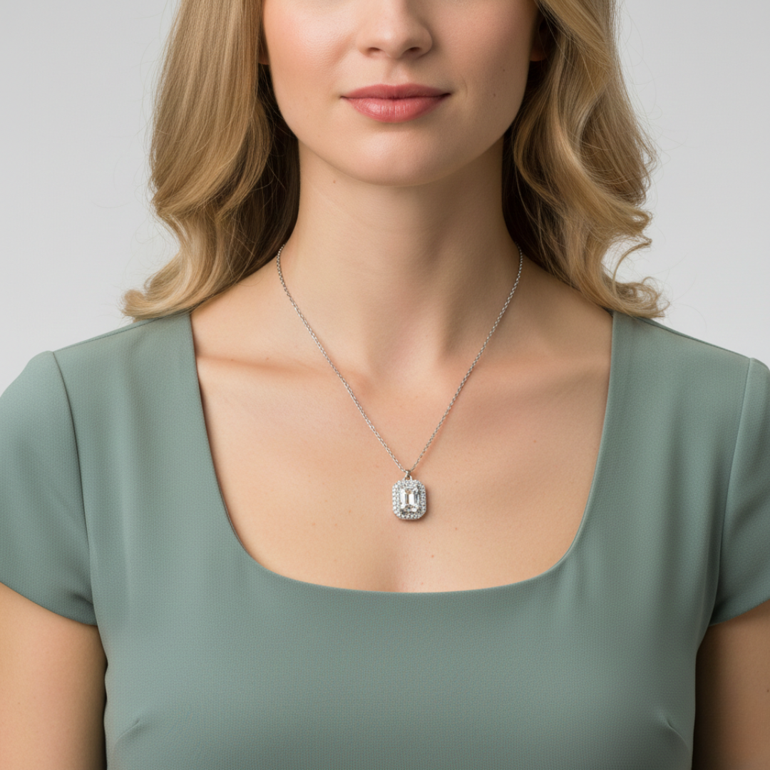 Woman wearing a green top and silver necklace with a large clear crystal pendant on a plain background