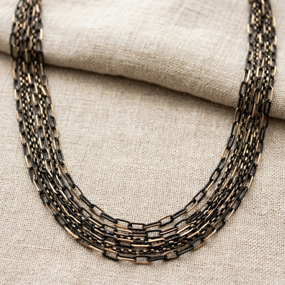 Multi-layered black and gold tone chain necklace on a textured fabric background