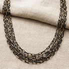 Multi-layered black and gold tone chain necklace on a textured fabric background