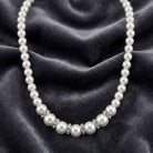 White Graduated Faux Pearl Strand And Crystal Necklace on a dark fabric background