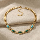 Gold chain bracelet with green and turquoise stones on a beige fabric background