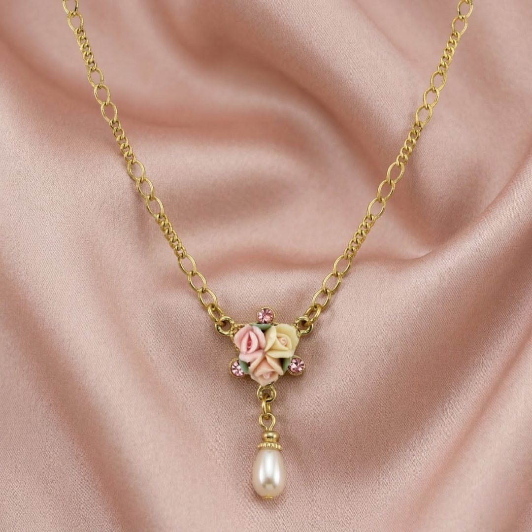 Gold necklace with a floral porcelain rose and faux pearl drop pendant on a pink fabric background