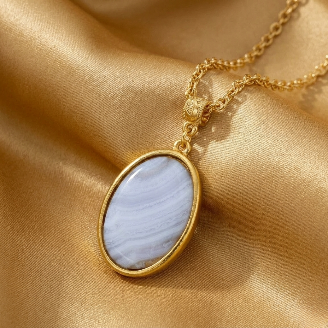 Gold necklace with a blue agate gemstone pendant on a gold fabric background