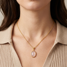 Gold necklace with a Rose Quartz gemstone pendant worn by a person in a beige sweater.