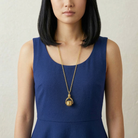 Woman wearing a blue dress and gold spinner pendant necklace against a neutral background