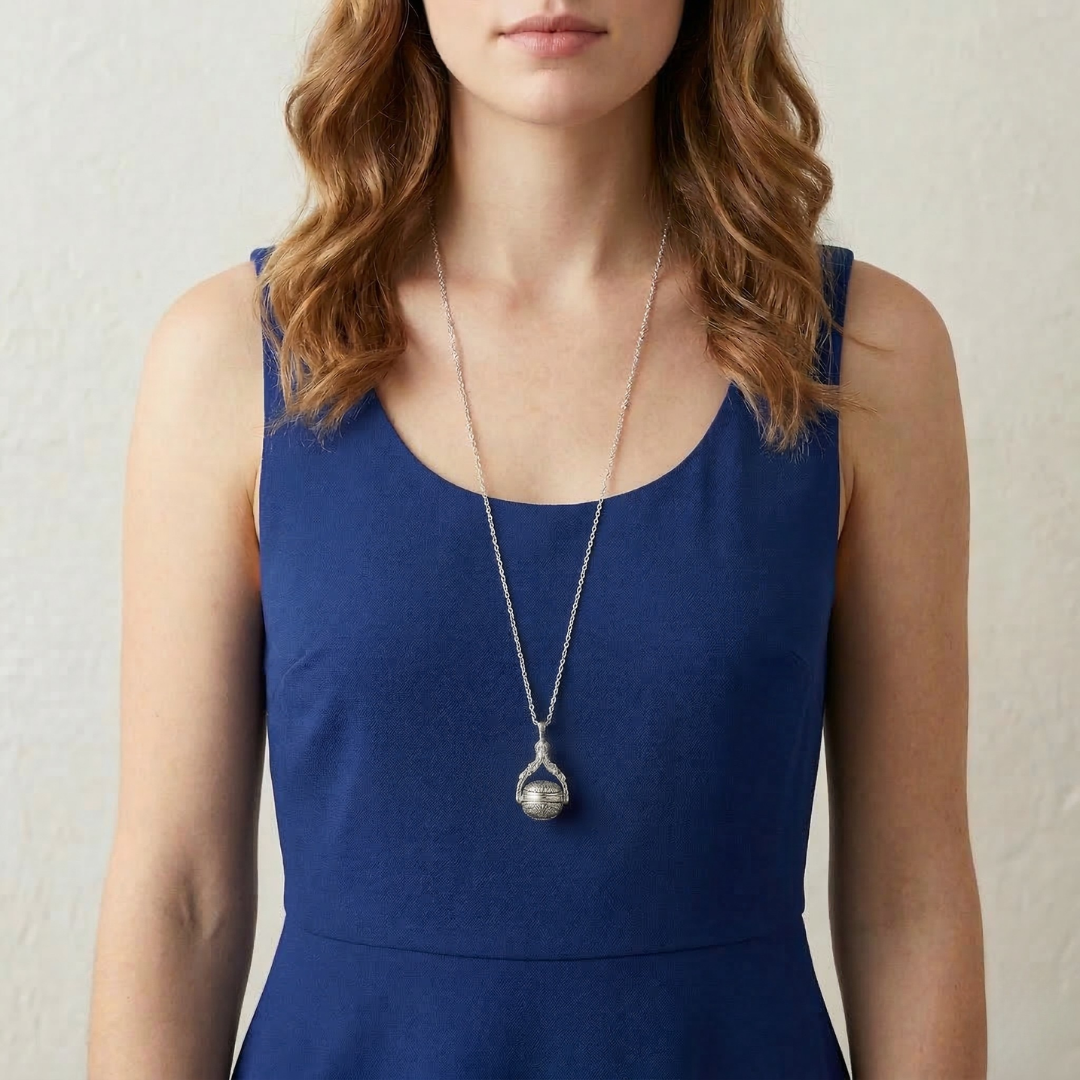 Woman wearing a blue dress with a long silver spinner pendant necklace against a neutral background