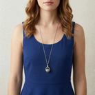 Woman wearing a blue dress with a long silver spinner pendant necklace against a neutral background