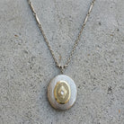 Necklace with an oval locket pendant featuring a gold design on a concrete surface