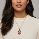 Woman wearing a gold necklace with a light red pendant against a neutral background