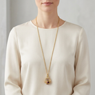 Person wearing a gold necklace with a three-sided spinner pendant on a plain background