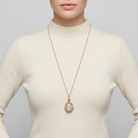 Person wearing a long gold necklace with a clear crystal spinner pendant on a plain background