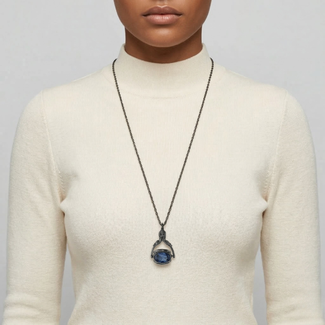 Person wearing a long necklace with a blue crystal spinner pendant on a plain background