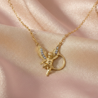Gold necklace with a winged angel pendant on a pink fabric background