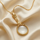 Gold necklace with a magnifying glass pendant on a beige fabric background