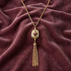 Manor House Ivory 3-Sided Roses Spinner Tassel Y-Necklace on a maroon fabric background