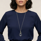 Woman in a navy outfit wearing a silver necklace with a cat magnifying glass pendant.