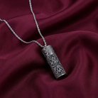 Silver necklace with an intricate vial pendant on a maroon fabric background