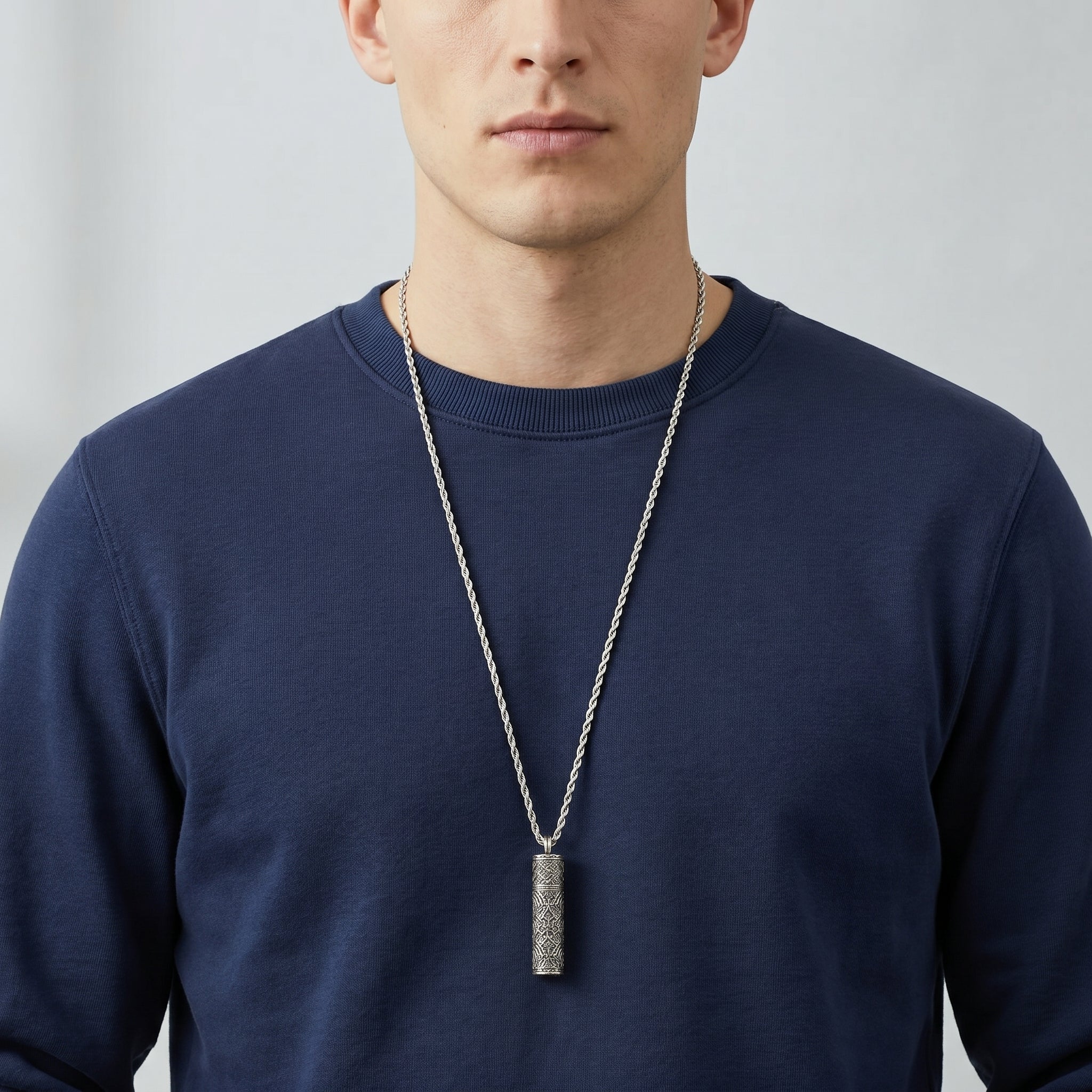 Man wearing a navy blue sweater with a silver vial pendant necklace against a plain background