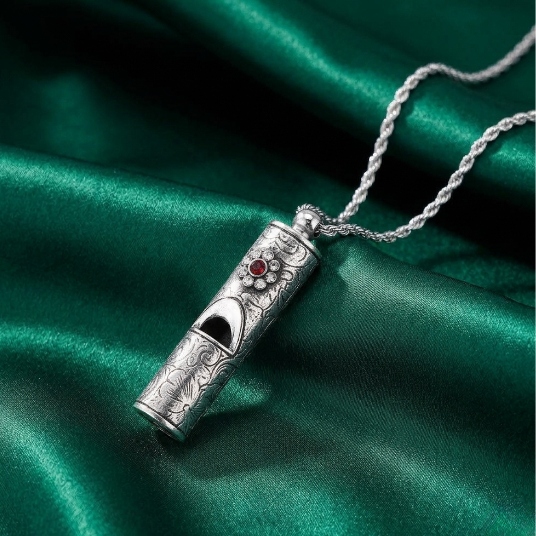 Silver whistle pendant and red and clear crystals with chain on a green satin background