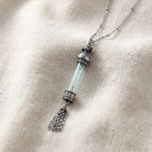 Antiqued Dog Light Blue Crystal Glass Vial Tassel Necklace on light linen fabric