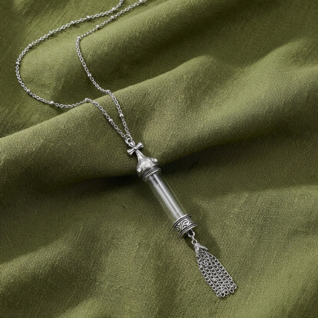 Silver tone cross vial pendant necklace resting on green colored cloth