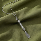 Silver tone cross vial pendant necklace resting on green colored cloth