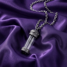 Silver necklace with a cylindrical glass vial pendant on purple fabric