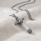 Cross glass vial pendant necklace resting on light colored linen