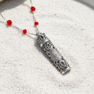 Silver Tone Filigrana Glass Vial Red Beaded Necklace resting neatly on fine white sand