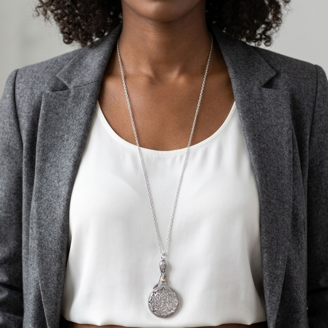 Person wearing a silver necklace with a sliding magnifying glass pendant against a neutral background