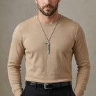 Man wearing a beige long-sleeve shirt with a horse whistle pendant necklace against a neutral background