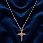 Gold necklace with purple stones and a cross pendant on a blue fabric background