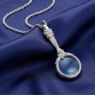 Silver necklace with a magnifying glass pendant on a blue fabric background