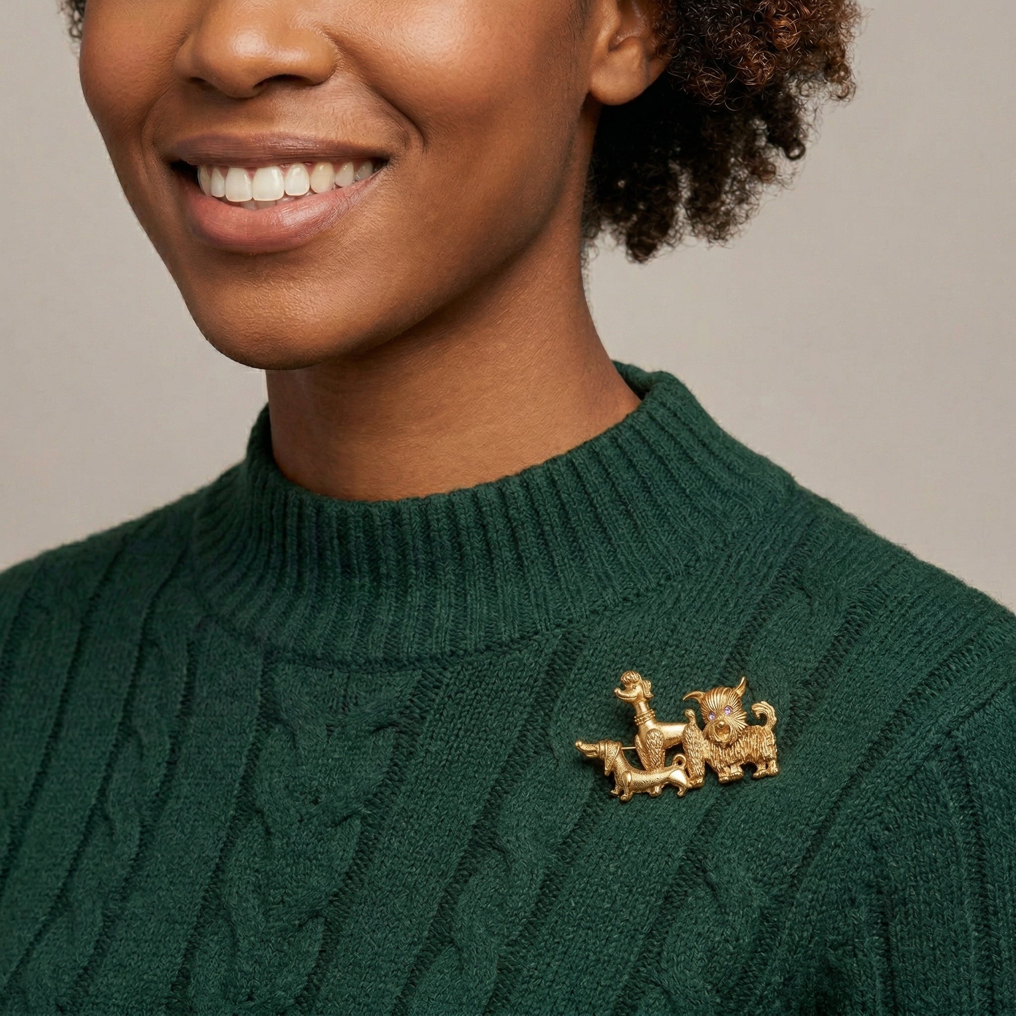 Woman wearing a green sweater with a gold brooch with three dogs on a neutral background