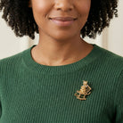 Woman wearing a green sweater with a cat on a rocking chair brooch, against a neutral background