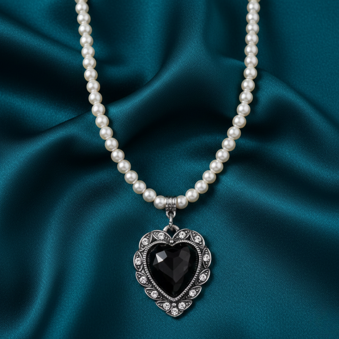 Faux pearl necklace with a black heart pendant on a teal fabric background