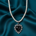 Faux pearl necklace with a black heart pendant on a teal fabric background