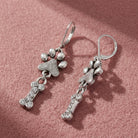 Paw & Clear Crystal Bone Dangling Earrings resting on pink felt
