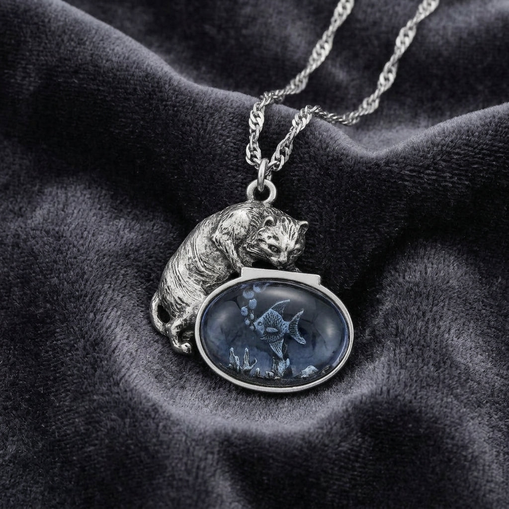 Whimsical Cat & Blue Fish Pendant Necklace on a dark fabric background