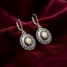 Pair of silver earrings with floral designs on a dark red fabric background