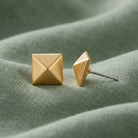 Gold Pyramid Post Earrings displayed on a textured sage green fabric background.