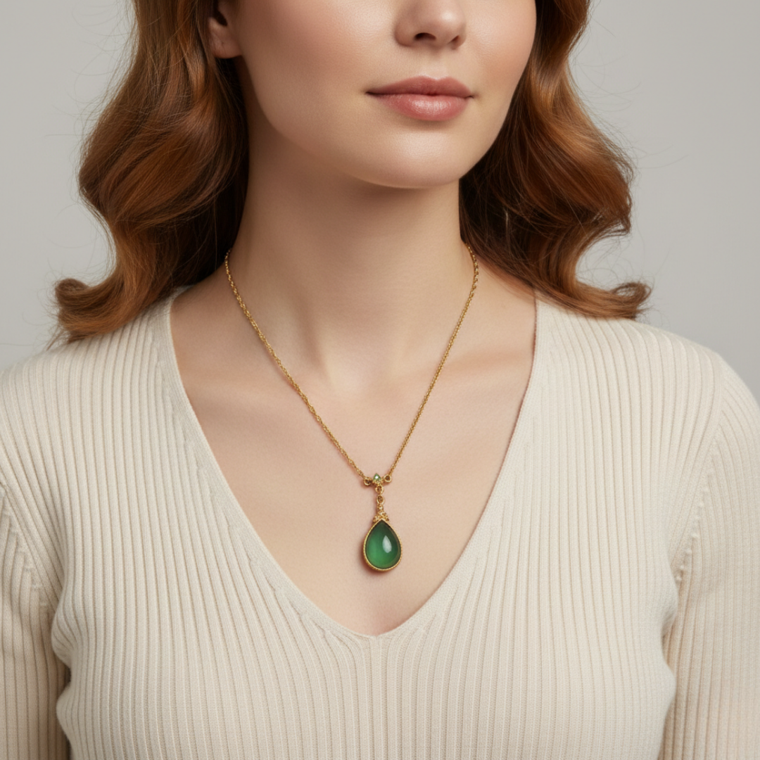Woman wearing a gold necklace with a green pendant against a neutral background