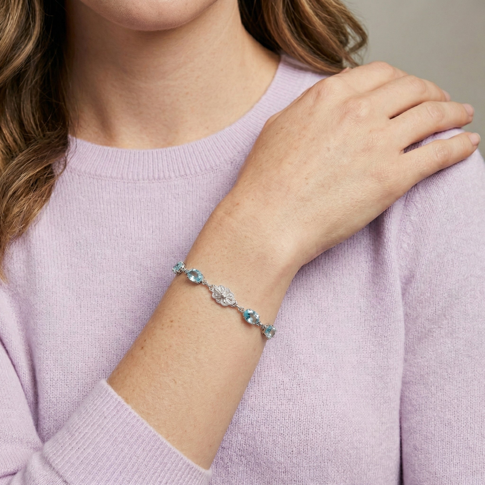 Person wearing a bracelet with blue crystals on a light purple sweater