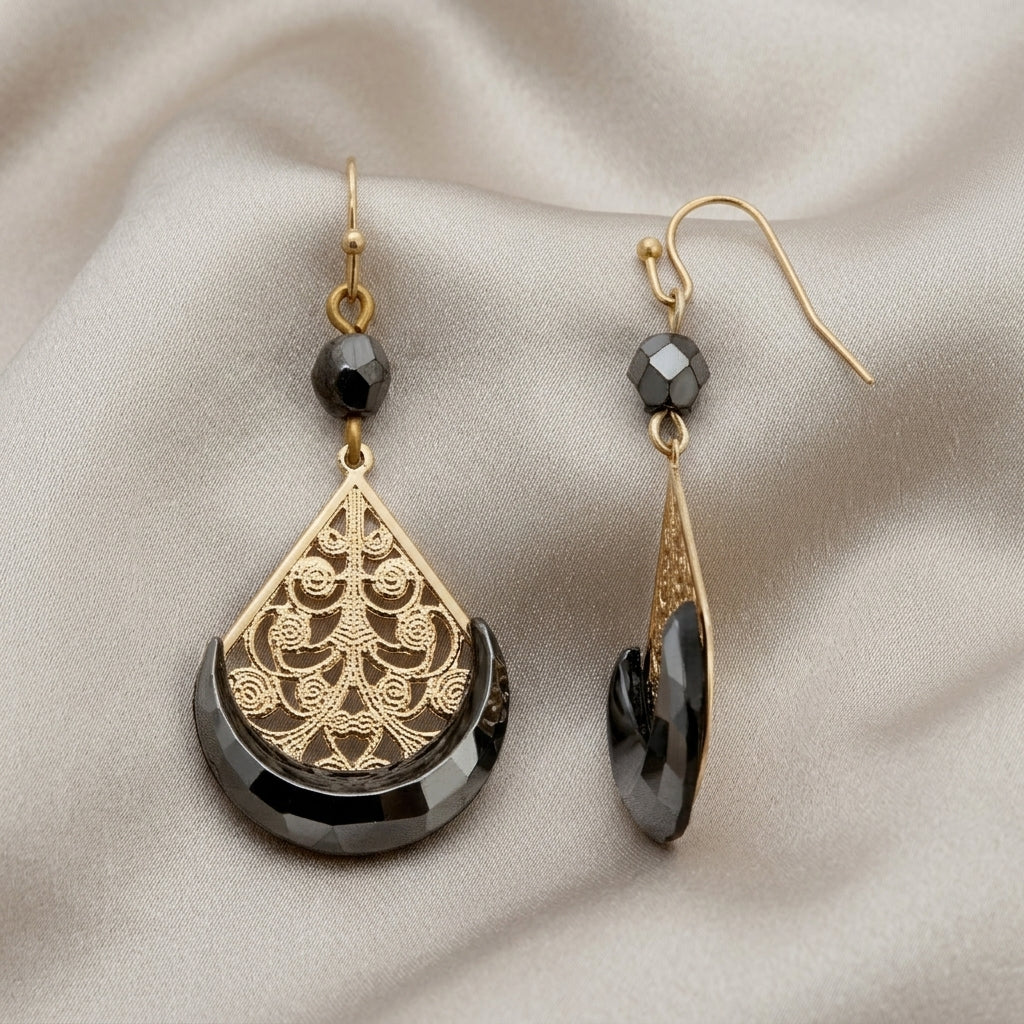 Gold tone filigree earrings with hematite beads and design resting on light colored satin fabric 
