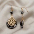 Gold tone filigree earrings with hematite beads and design resting on light colored satin fabric 