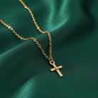 Gold necklace with a cross pendant on a green fabric background