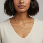 Woman wearing a gold necklace with a cross pendant against a neutral background