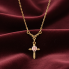 Gold necklace with a cross pendant featuring a porcelain rose on a maroon fabric background