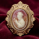 Decorative cameo brooch with intricate design on a red fabric background